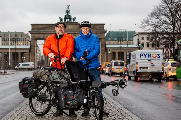 Zwei Männer stehen mit einem Tandem vor dem Brandenburger Tor in Berlin