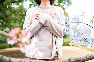 Bild Selbsthilfe, Frau steht in einem Park, ihr Gesicht ist nicht zusehen, die Hände sind entspannt vor dem Brustkorb gekreuzt