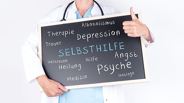 Bild Was ist Selbsthilfe, Arzt hält Tafel mit Wörtern wie Selbsthilfe und anderen gesundheitsbezogenen Begriffen